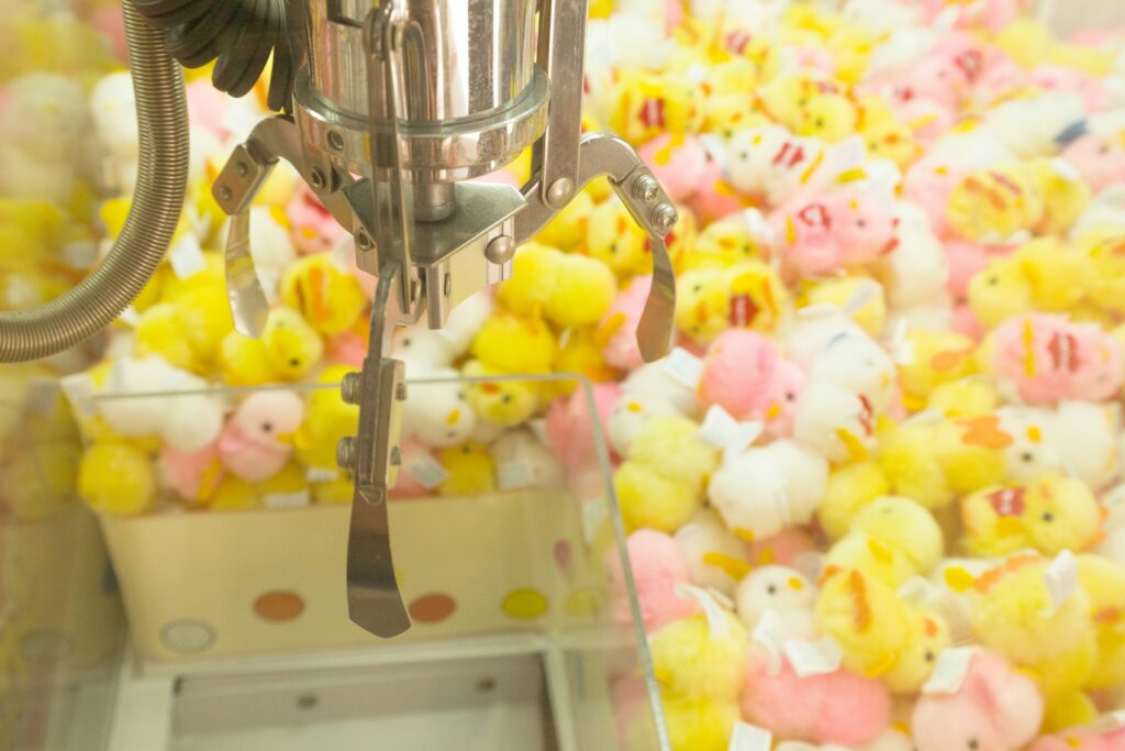 how to win claw machine showing a claw gripping a stuffed animal prize above the prize chute in an arcade claw machine representing tips and strategies for winning at claw machines